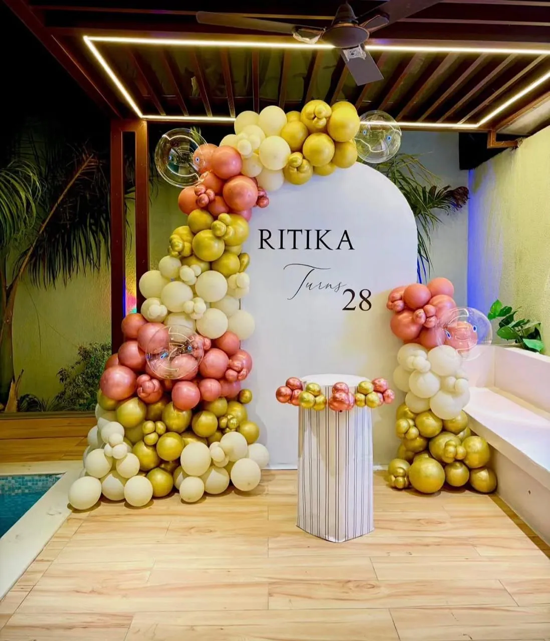 Gold and blush balloon arch set up beside a poolside terrace